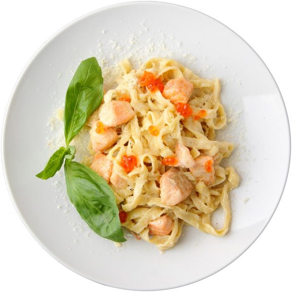 Plate of pasta in cream sauce with peppers, chicken, and garnished with basil leaves.